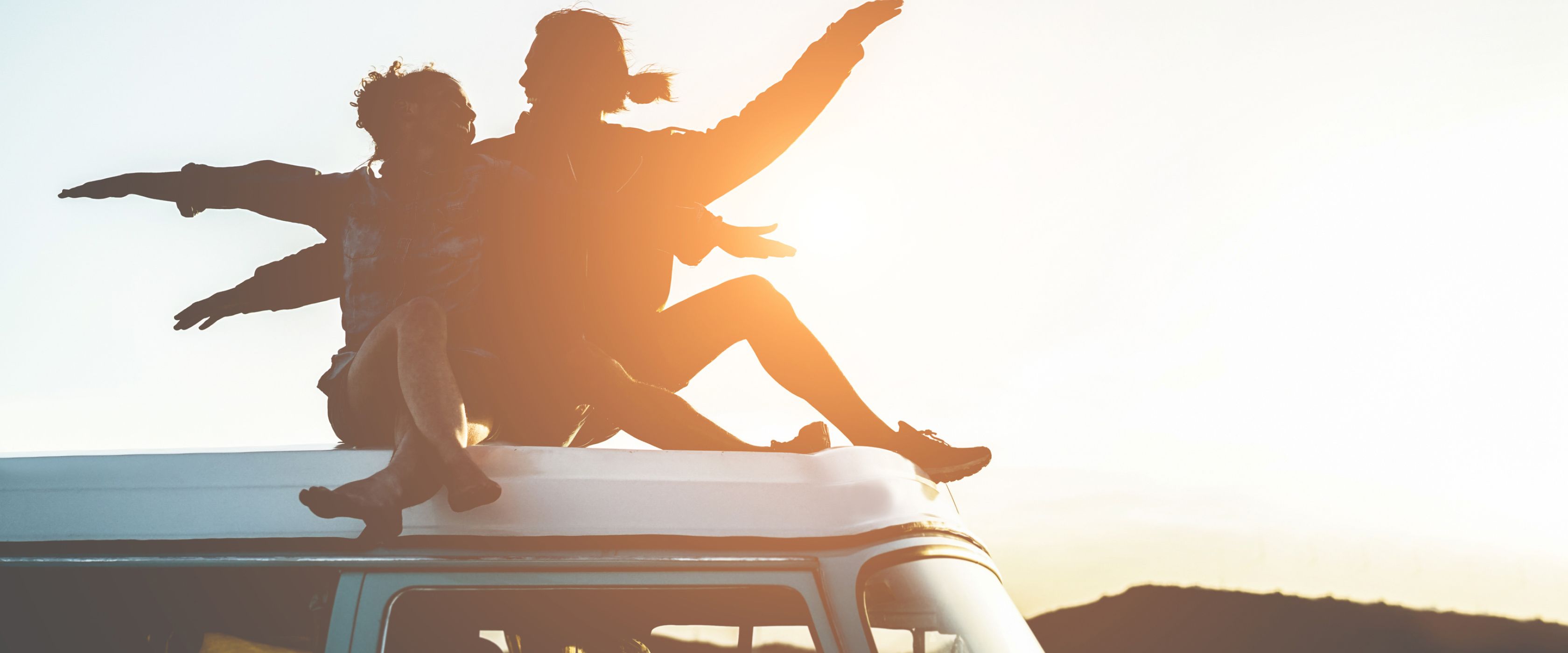 Two people sitting on a Van in the sunset