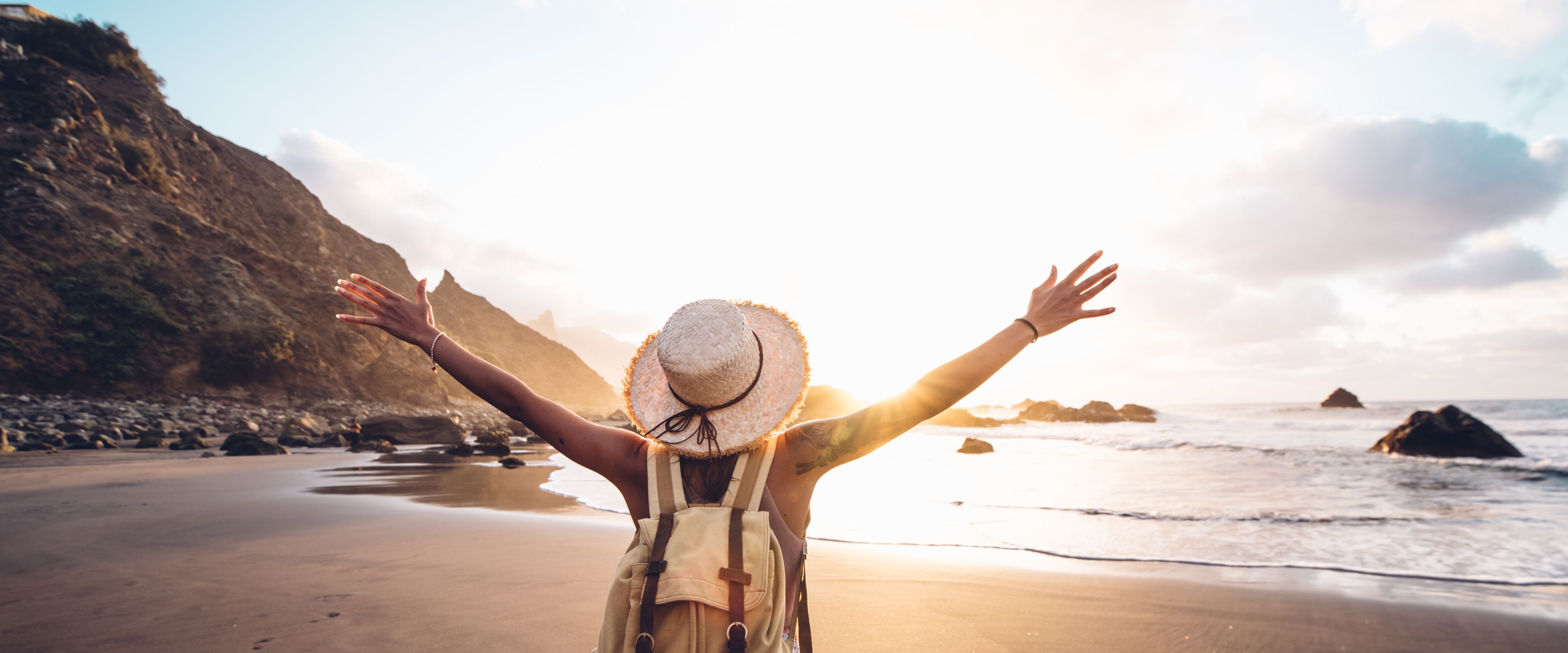 Woman standing on beach with hands raised