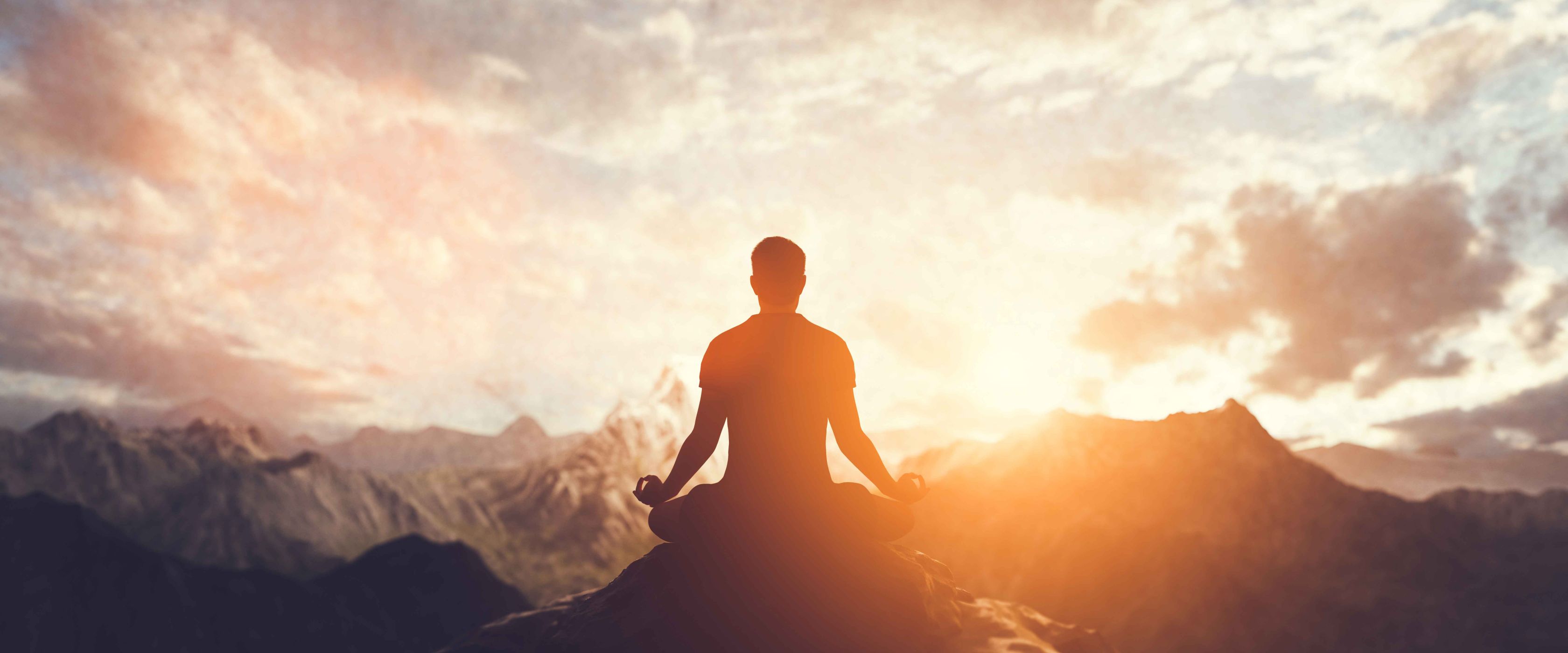 Man meditating on cliff ledge 