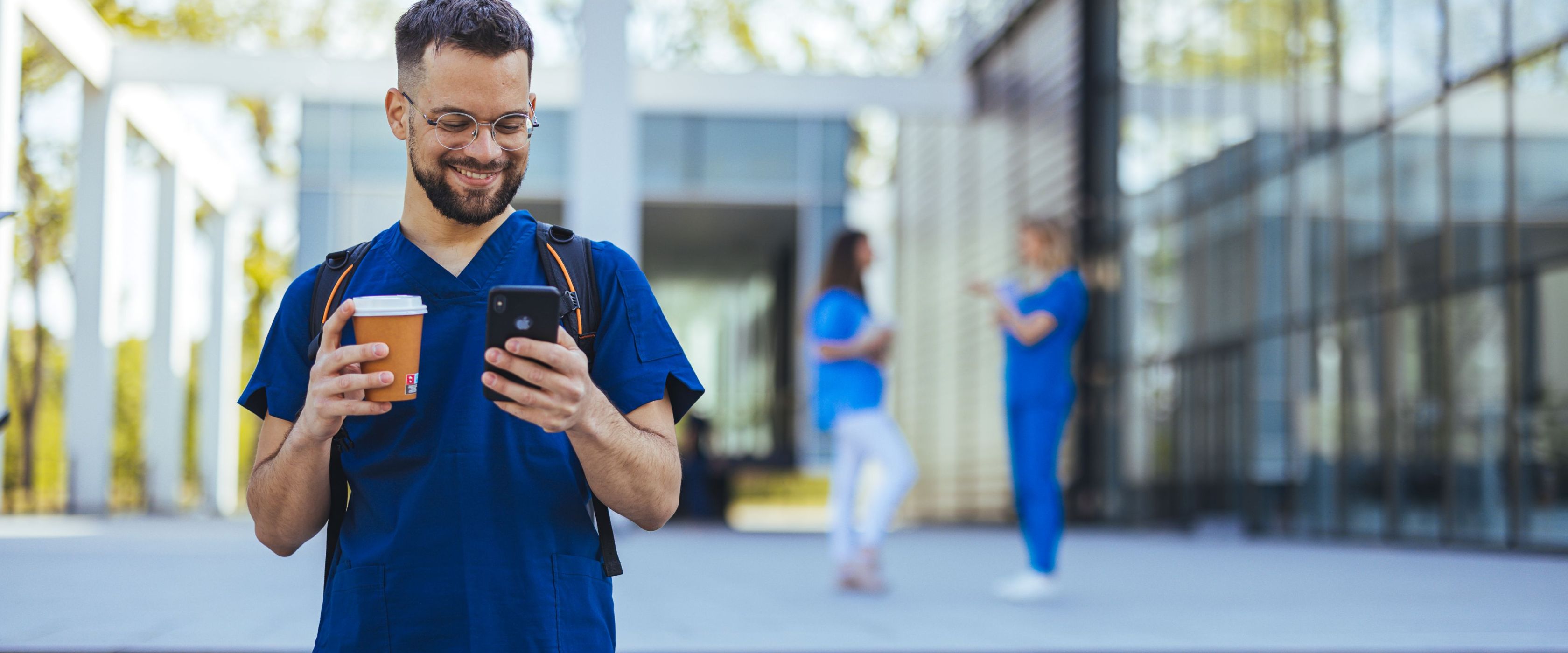 Male healthcare professional smiling at his phone drinking coffee