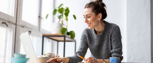 Young nurse researching travel assignments and Nurses Week 2025 freebies on a laptop in a bright, modern home workspace.