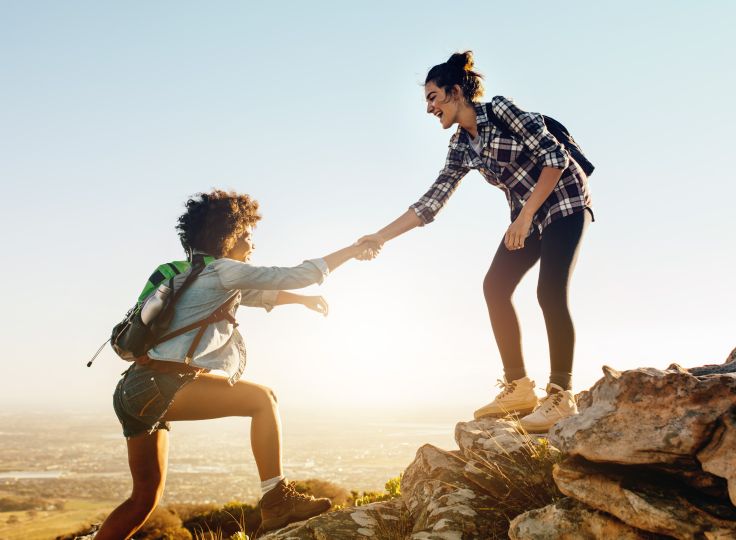 Two women helping each other up a mountain