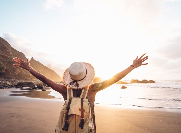 Woman standing on beach with hands raised