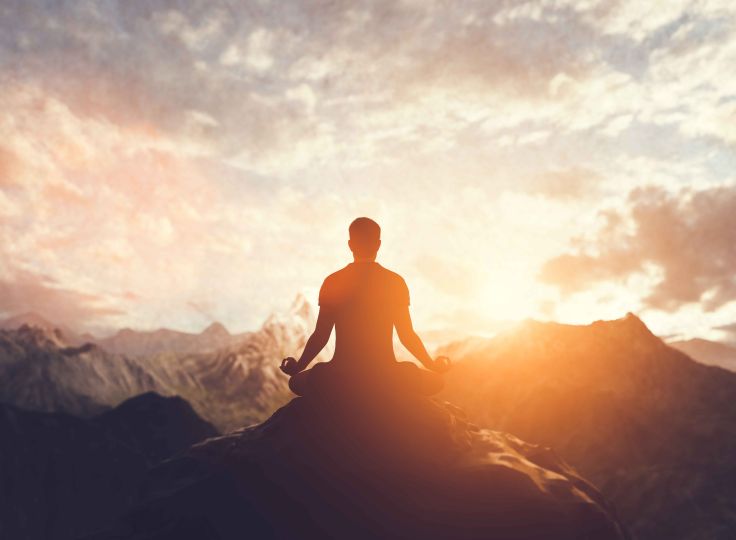 Man meditating on cliff ledge 