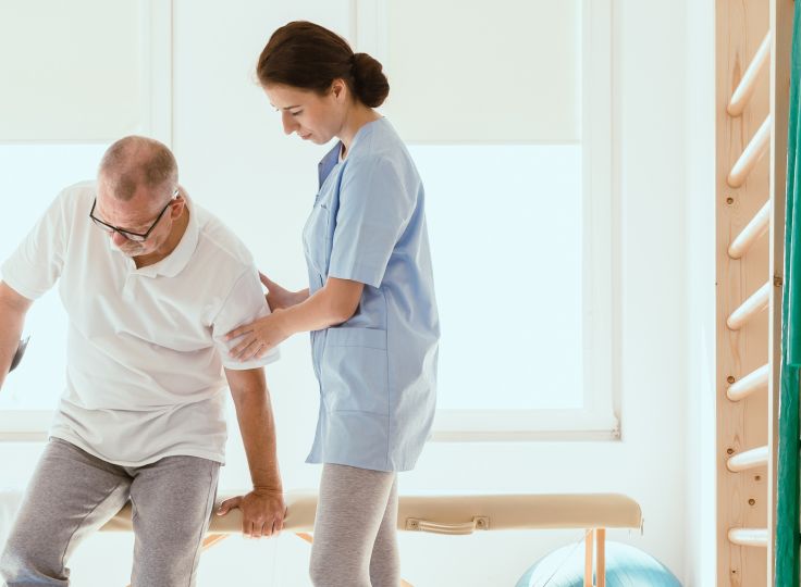 Female physiotherapist assisting elderly man with mobility training in a bright rehabilitation clinic. Ideal for senior physical therapy, stroke recovery, and in-home care services.