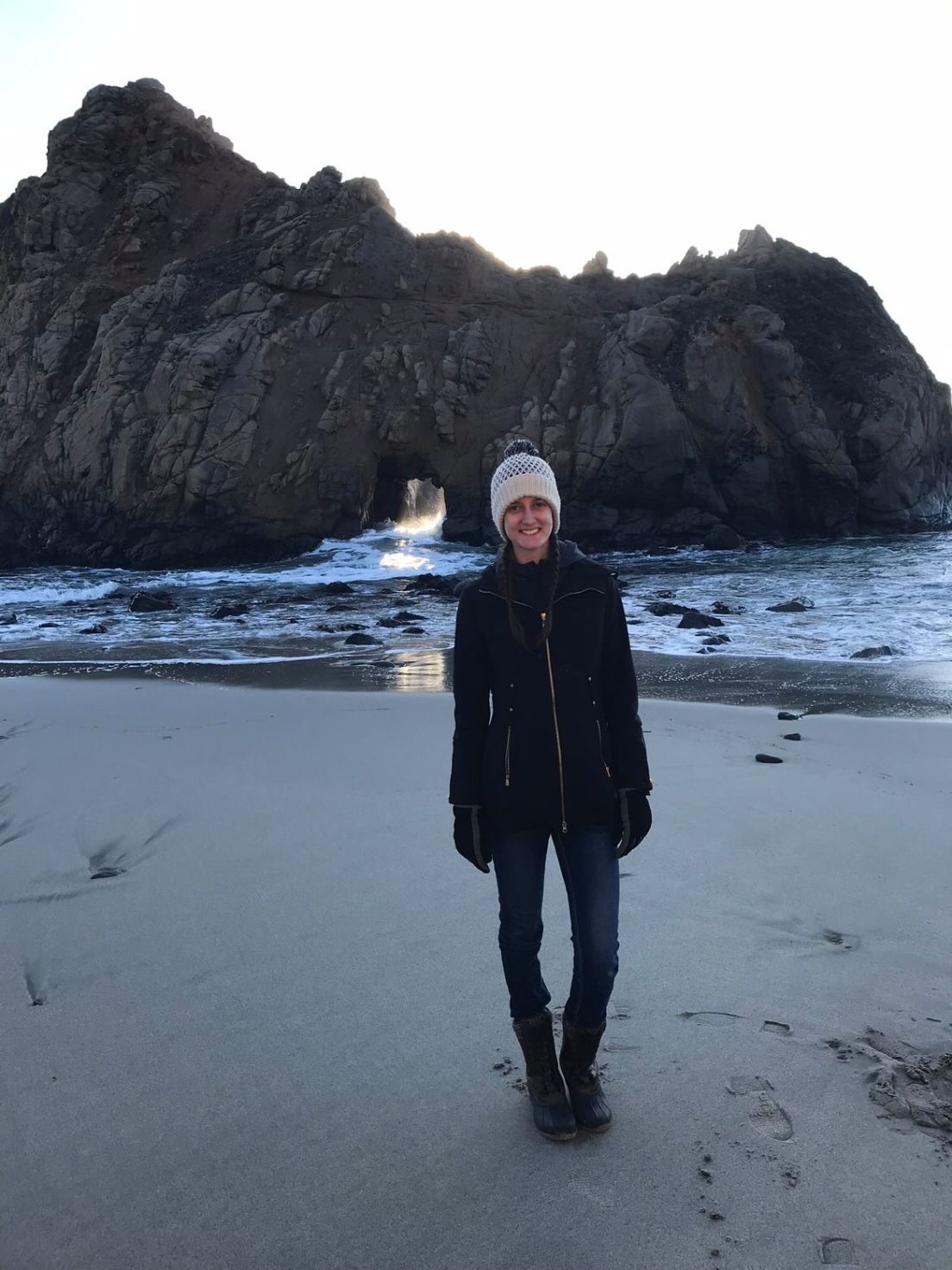 Woman standing on beach in front of rock formation