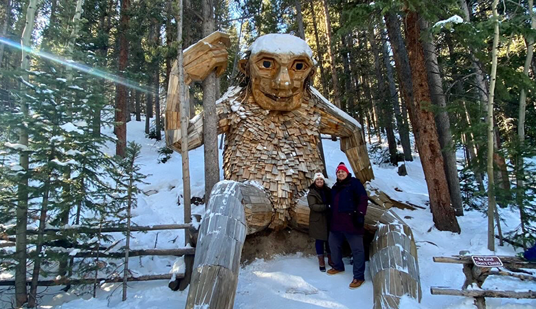 Two people standing in front of wooden sculpture 