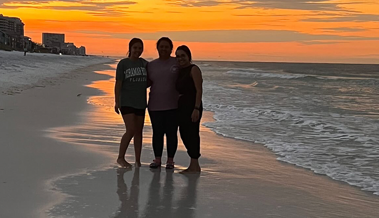 Three people standing on beach at sunset
