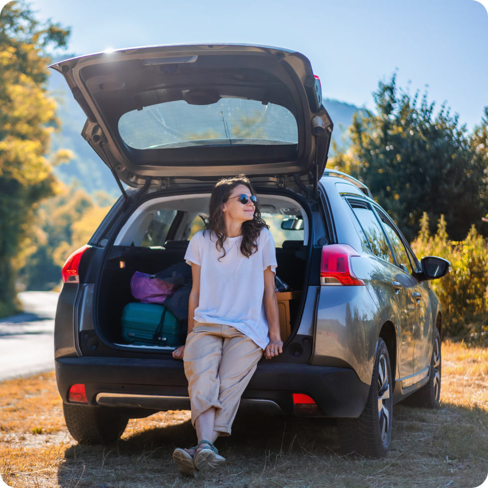A clinician rests on the bumper of her car while before taking a hike during her time off