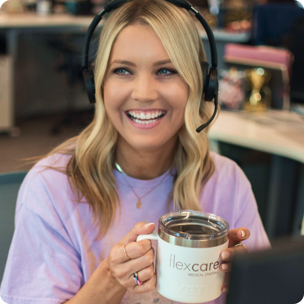 A smiling FlexCare Staffing recruiter holds a coffee mug while speaking over a headset microphone