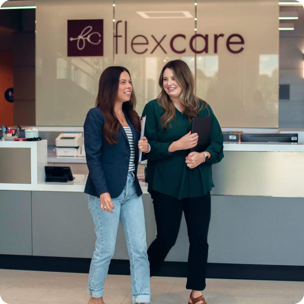 Two women with clipboards walk past a flexcare sign